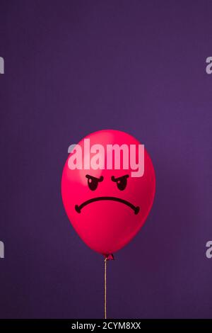 Photo d'un ballon rouge avec visage en colère sur fond violet. Notion de colère et d'ennui Banque D'Images