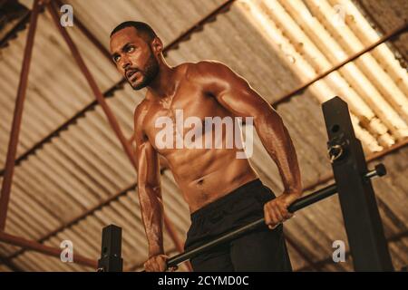 Homme musclé faisant de l'exercice sur le bar horizontal dans le studio de fitness. Homme fort s'exerçant sur la barre horizontale à l'intérieur de l'ancien entrepôt. Banque D'Images