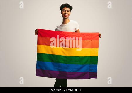 Homme gay souriant avec drapeau de fierté. Homme fluide de genre tenant un drapeau lgbt sur fond blanc. Banque D'Images
