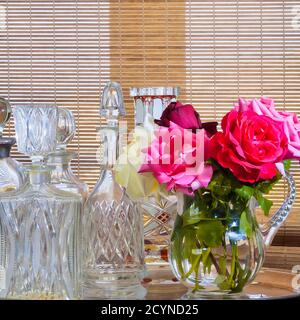 Fleur rose dans un pot à eau en cristal. Carafes en cristal vintage vides sur la gauche. Image de stock Banque D'Images