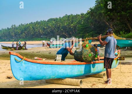 Les pêcheurs portent le filet de leur bateau avec un poteau d'épaule à la belle plage de Kizhunna, au sud de Kannur sur la côte du Keralan Nth; Kannur, Kerala, Inde Banque D'Images