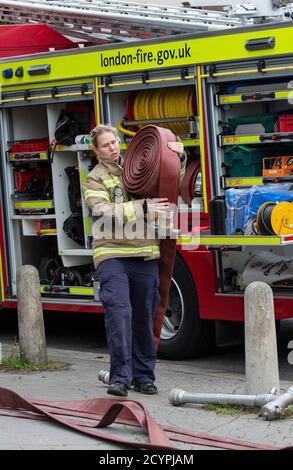 Une pompier lance le tuyau avec la brigade de pompiers de Londres pour assister à un incendie de maison dans une rue résidentielle, sud de Londres, Angleterre, Royaume-Uni Banque D'Images