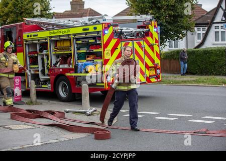 Une pompier lance le tuyau avec la brigade de pompiers de Londres pour assister à un incendie de maison dans une rue résidentielle, sud de Londres, Angleterre, Royaume-Uni Banque D'Images