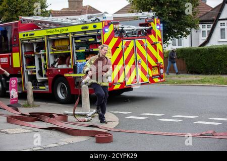 Une pompier lance le tuyau avec la brigade de pompiers de Londres pour assister à un incendie de maison dans une rue résidentielle, sud de Londres, Angleterre, Royaume-Uni Banque D'Images