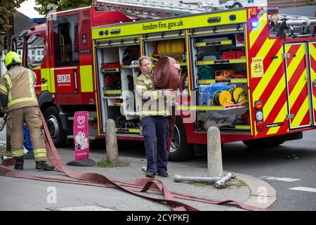 Une pompier lance le tuyau avec la brigade de pompiers de Londres pour assister à un incendie de maison dans une rue résidentielle, sud de Londres, Angleterre, Royaume-Uni Banque D'Images