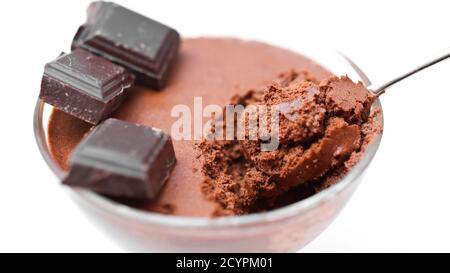 Bol transparent avec mousse au chocolat et cuillère à café et trois morceaux de chocolat noir isolé sur un fond blanc gros plan Banque D'Images