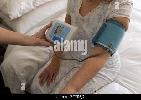 Femme caucasienne âgée à domicile visitée par une infirmière caucasienne, vérifiant la tension artérielle. Soins médicaux à domicile pendant la quarantaine du coronavirus Covid 19 Banque D'Images