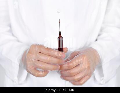Médecin ou laboratoire scientifique dans un équipement de protection individuelle tenant une seringue remplie de sang, en se concentrant sur une goutte unique qui s'écoule de l'extrémité de l'aiguille Banque D'Images