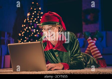 Un elfe fou et choqué a lu x-mas félicitations pour le port d'un ordinateur portable costume vert dans la maison du soir de noël à l'intérieur avec éclairage Banque D'Images