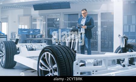 Ingénieur concepteur automobile regardant le dessin technique d'un prototype de châssis de voiture électrique sur une tablette. Dans le concept d'installation de laboratoire d'innovation Banque D'Images