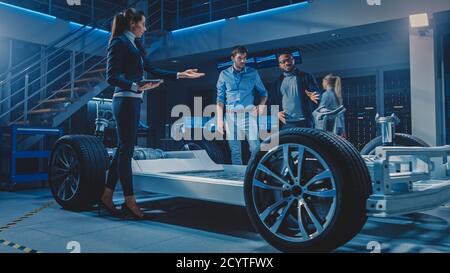 Équipe internationale d'ingénieurs concepteurs d'automobiles parlant et concevant une voiture électrique autonome. Le châssis de la plate-forme du véhicule comporte des roues, des moteurs et une batterie Banque D'Images