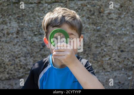 Un garçon de six ans regarde à travers une loupe dans son jardin arrière tout en cherchant des insectes, Angleterre, Royaume-Uni Banque D'Images