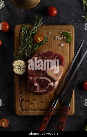 Steak de bœuf marbré cru sur l'os avec de l'ail au romarin et tomates cerises sur fond sombre Banque D'Images