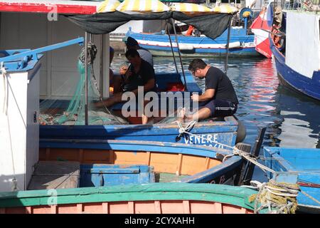 Les pêcheurs qui font leurs filets de pêche sur les ponts de leurs Bateaux dans le port dans la vieille ville de Trapani Sicile Banque D'Images