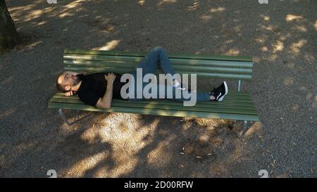 Les hommes font une sieste sur un banc dans le parc. Banque D'Images