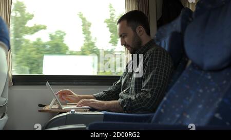 Homme charmant utilisant une tablette numérique lors de ses déplacements en train. Banque D'Images