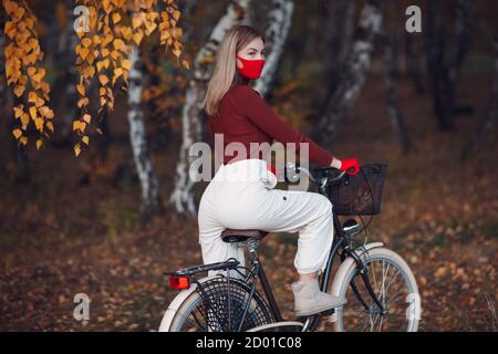 Jeune femme à vélo avec des gants rouges et un masque facial au parc d'automne Banque D'Images