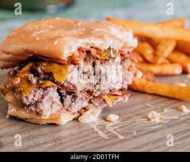 Cheeseburger au bacon à moitié mangé avec frites sur une assiette en bois Banque D'Images