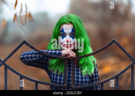 Portrait rapproché d'une fille aux cheveux verts en robe à l'enne avec maquillage de joker sur un fond marron flou. Banque D'Images
