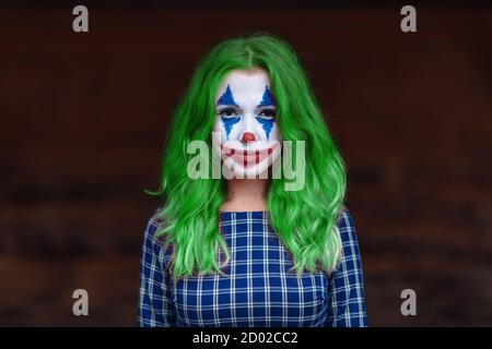 Portrait rapproché d'une fille aux cheveux verts en robe à l'enne avec maquillage de joker sur un fond marron flou. Banque D'Images