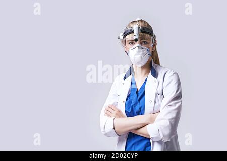 Médecin ORL confiant portant une lanterne chirurgicale à tête de projecteur, un masque facial de protection et des lunettes. Portrait de la femme otolaryngologiste debout bras Banque D'Images