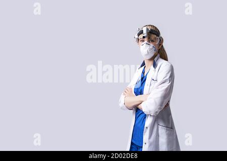 Médecin ORL confiant portant une lanterne chirurgicale à tête de projecteur, un masque facial de protection et des lunettes. Portrait de la femme otolaryngologiste debout bras Banque D'Images