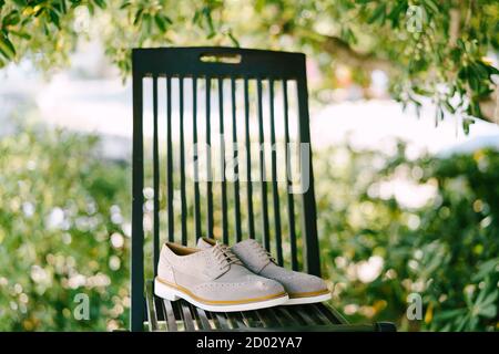 Chaussures oxford grises pour hommes, avec semelles blanches, sur une chaise en bois dans le jardin, sur fond vert. Banque D'Images