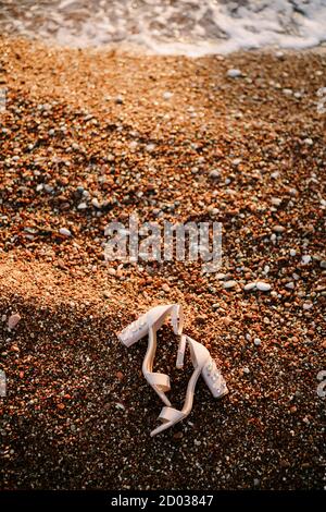 Sandales de mariée avec talons épais décorées de pierres sur une plage de galets sur la mer. Banque D'Images