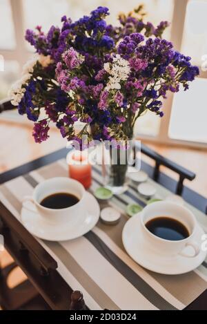 Deux tasses de café et bouquet de fleurs roses violettes dans un vase Banque D'Images