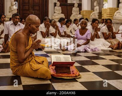 Kandy, Sri Lanka - 09-03-24 - Monk mène des fidèles dans la prière dans le Temple. Banque D'Images