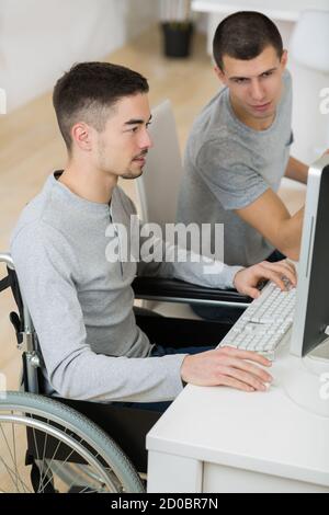 deux jeunes hommes utilisant un ordinateur, un en fauteuil roulant Banque D'Images