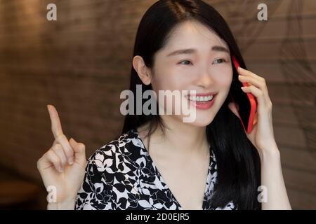 Une femme chinoise américaine très heureuse utilisant un smartphone rouge dans un café Banque D'Images