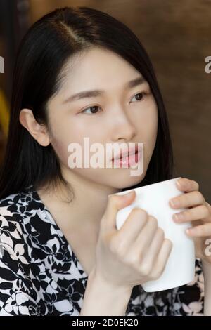 Femme chinoise américaine tenant une tasse de café dans un café-restaurant avec photocopieur Banque D'Images