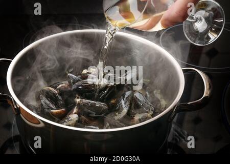 Les moules à la vapeur dans une casserole sont déglacés avec du vin blanc, concept de cuisine pour un délicieux plat de fruits de mer, foyer sélectionné, profondeur de champ étroite Banque D'Images