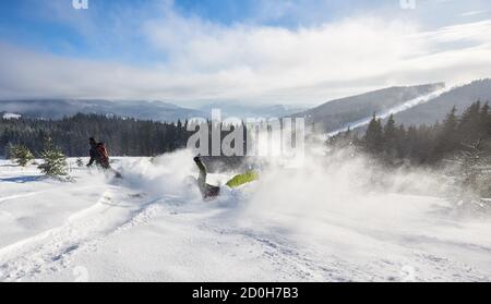 Course de ski depuis la haute montagne. Le skieur fait des manœuvres malheureuses dans les virages et en tombant sur la neige. Vue arrière de deux skieurs. Dépasser, tomber, vaincre concept. Vue panoramique sur la montagne. Banque D'Images