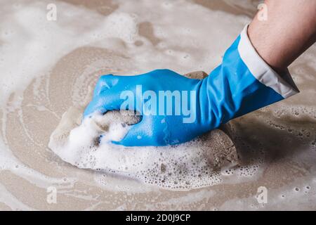 La main de l'homme portant des gants en caoutchouc bleu utilise une éponge pour nettoyer le sol carrelé. Banque D'Images