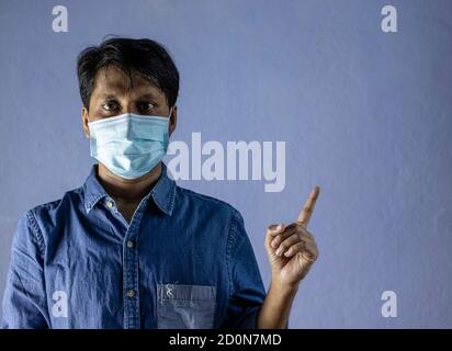Un Indien portant un masque nasal chirurgical, regardant l'appareil photo et pointant vers la gauche pour la protection contre le virus corona ou Covid-19 sur fond blanc Banque D'Images