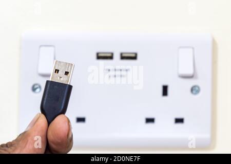 Homme tenant la broche de la fiche USB devant un module double Prise uk avec ports USB Banque D'Images