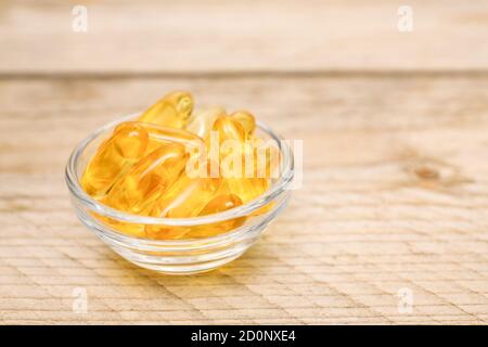 bol en verre avec capsules d'huile de poisson sur fond en bois Banque D'Images
