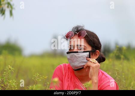 Une jeune femme indienne élégante modèle posant dans un champ portant un masque brun pour prévenir la maladie de corona, concept pour protéger les agriculteurs, les ouvriers, OUTD Banque D'Images