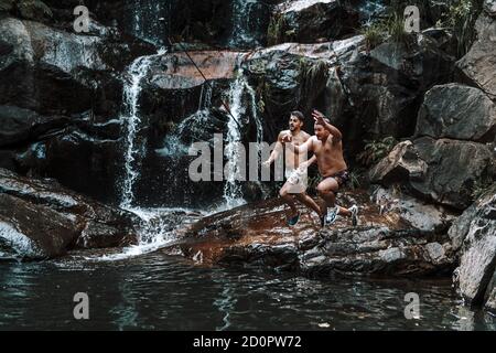 Photo au niveau des yeux d'amis fous de sexe masculin dans des maillots de bain qui sautent vers eau du lac Banque D'Images