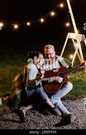 Jeune couple sur un pique-nique avec une guitare prendre un selfie ou communication vidéo avec des amis ou des parents Banque D'Images