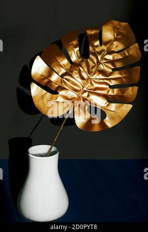 Feuille de monstère tropicale dorée tendance dans un vase blanc sur noir arrière-plan Banque D'Images