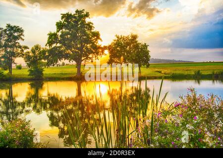 Coucher de soleil spectaculaire et vif se reflétant dans l'étang. Le soleil couchant brille à travers les arbres. République tchèque Banque D'Images