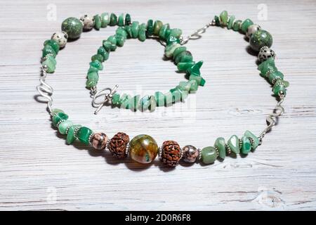 collier fait à la main de pierres précieuses en polishedgreen aventurine, balle d'agate fissurée, aplite, rhodonite et rudraksha sur une table en bois gris Banque D'Images