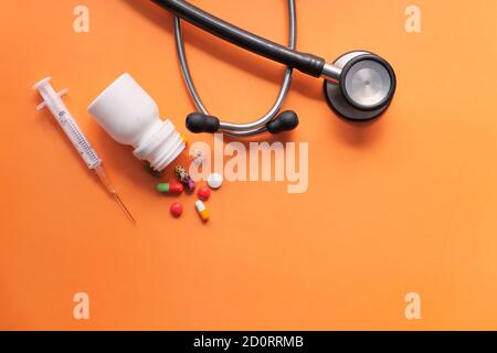 composition plate du stéthoscope , de la seringue et des pilules sur fond orange Banque D'Images
