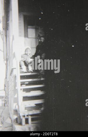 Belle photographie en noir et blanc vintage des années 1970 d'une jeune fille assise dans les escaliers avec son grand-père. Banque D'Images