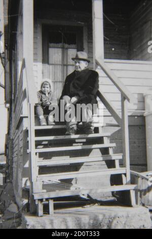 Belle photographie en noir et blanc vintage des années 1970 d'une jeune fille assise dans les escaliers avec son grand-père. Banque D'Images