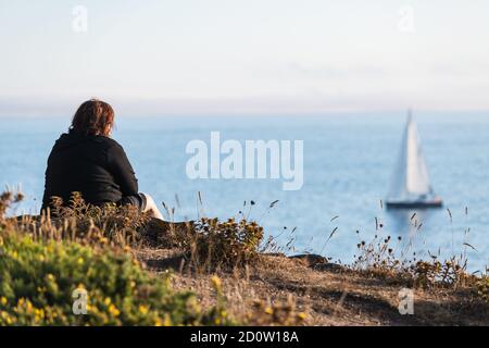 Une femme solitaire d'âge moyen regarde un bateau à voile loin de l'île d'Ons dans la Ria de Pontevedra en Galice au crépuscule. Banque D'Images