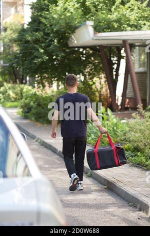 Jeune livreur marchant avec un sac thermal de nuit dans la rue de la ville. Homme de service de livraison pressé de livrer une commande. Le service de livraison va donner t Banque D'Images